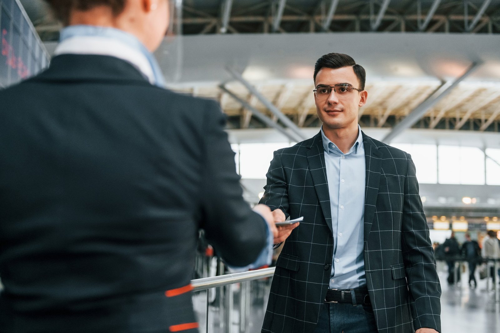 Giving the documents. Young businessman in formal clothes is in the airport at daytime